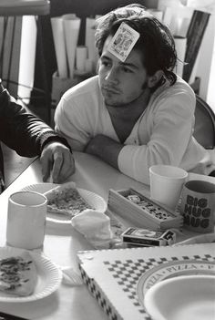 two men sitting at a table with plates of food and cups on top of them