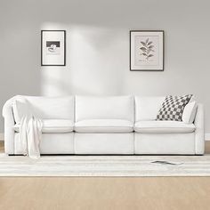 a white couch sitting on top of a hard wood floor next to a wall with pictures above it