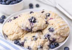 blueberry scones with icing on a plate next to a bowl of berries