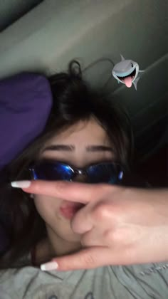 a woman wearing sunglasses and pointing her finger at the camera with an alien sticker above her head