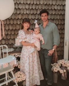 a man standing next to a woman holding a baby wearing a party hat and dress