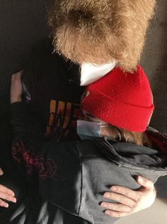 two people are hugging each other while one person is wearing a red beanie and the other wears a black shirt