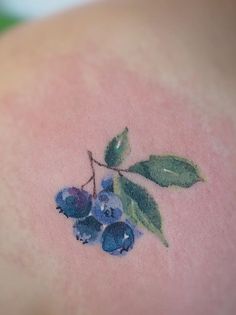 a small tattoo with blueberries and leaves on it