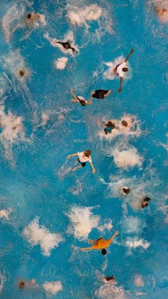 several people swimming in a pool with blue water and white clouds on the bottom half