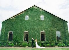 a bride and groom standing in front of a green building with ivy growing on it