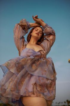 a woman in a purple dress poses for the camera with her hands behind her head