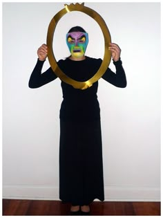 a woman in a black dress is holding up a circle with a mask on her face