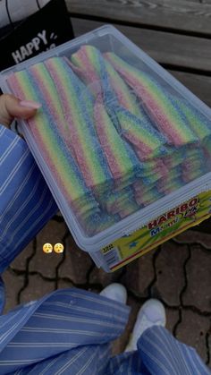 a person holding a plastic container filled with colored powdered food items on top of a wooden bench