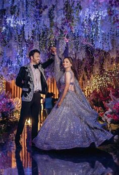 a man and woman dressed in formal wear standing next to each other under purple flowers