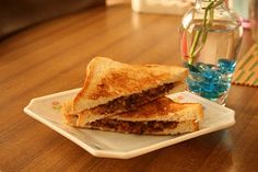 a sandwich cut in half on a plate next to a vase with water and flowers