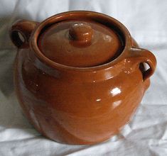 a brown pot with a lid sitting on a white sheet