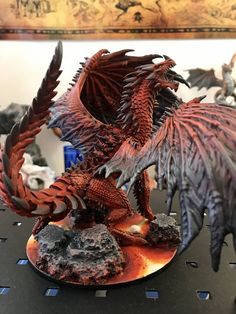 a red dragon figurine sitting on top of a table next to some rocks