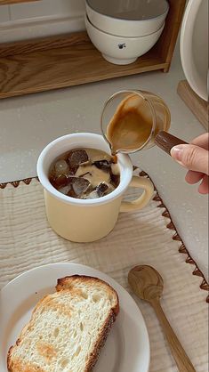 a person pouring soup into a bowl on top of a white plate next to a slice of bread