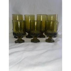 a set of six green glass cups sitting on top of a white cloth covered table