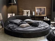 a large round bed in the middle of a living room with lots of pillows on it