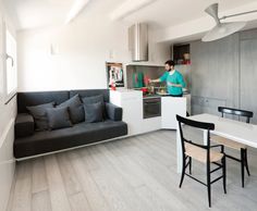 a woman standing in the kitchen next to a couch and table with chairs on it