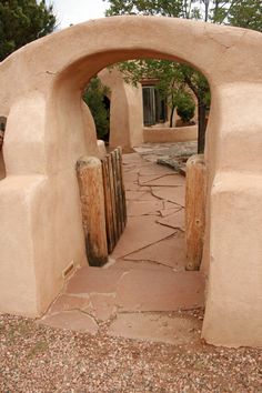 an arch in the side of a building with rocks around it and trees behind it