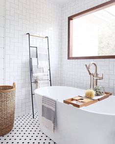 a white bath tub sitting under a window next to a sink and towel rack in a bathroom