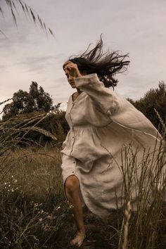 a woman is running through the grass with her hair blowing in the wind while wearing a white dress