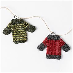 two knitted sweaters hanging from strings on a white surface, one is red and the other is green