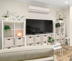 a living room with white furniture and a flat screen tv mounted on the wall above it