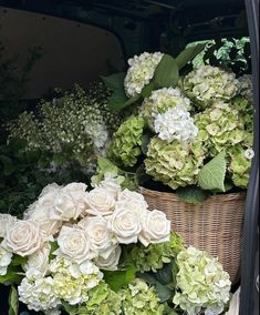 a basket filled with lots of white flowers next to green leaves and plants in the back of a truck