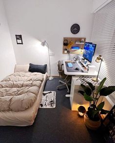 a room with a bed, desk and computer on the wall in it's corner