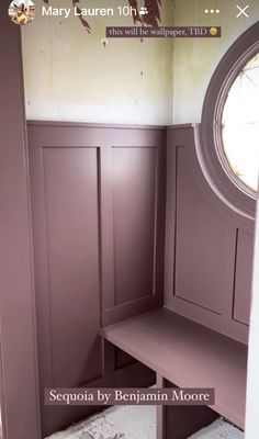 an empty room with purple painted walls and a bench in the corner, next to a round window