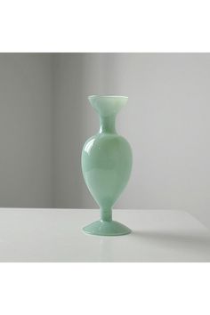 a light green vase sitting on top of a white table next to a wall in the background