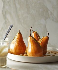 three pears on a plate next to a glass of milk