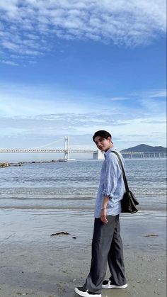 a man is walking on the beach with a bag in his hand while looking at the water