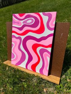 a pink and red painting sitting on top of a wooden stand in the middle of grass