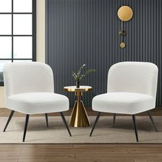 two white chairs sitting next to each other in front of a table with a vase on it