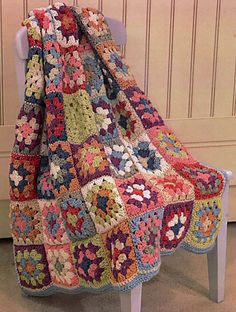 a crocheted blanket sitting on top of a white chair next to a wall