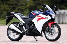 a red, white and blue motorcycle is parked on the brick floored area next to some trees