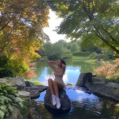 a woman sitting on top of a rock next to a river