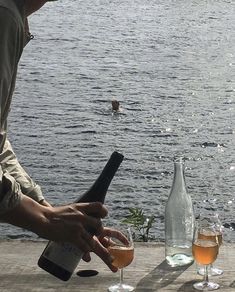 two glasses of wine are being poured in front of a man on the water's edge