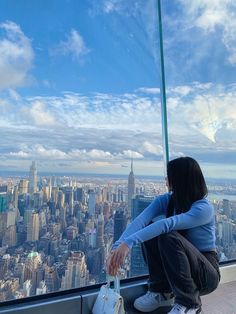 a woman sitting on top of a tall building looking out at the cityscape