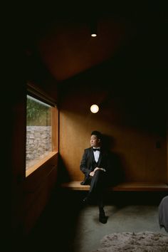 a man in a tuxedo is sitting on a bench looking out the window