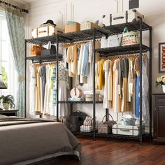 a bedroom with a bed, dresser and shelves filled with clothes on hangers next to a window