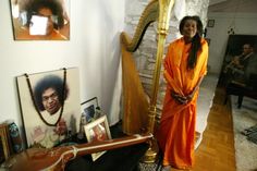 a woman in an orange dress standing next to a harp and pictures on the wall