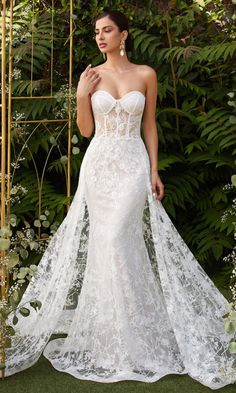 a woman in a white wedding dress standing next to a gold trellis and greenery