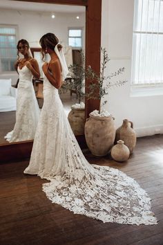 a woman standing in front of a mirror wearing a wedding dress and looking at her reflection