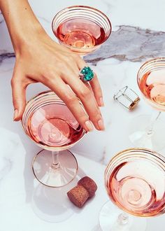 a woman's hand reaching for a green ring on top of some wine glasses