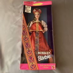 the barbie doll is in its box and has a red dress with gold trimmings