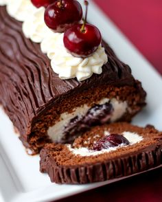 a piece of chocolate cake with cream and cherries on top, cut in half