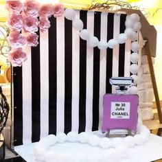 a chanel bottle sitting on top of a table next to flowers and balloons in front of a black and white striped backdrop