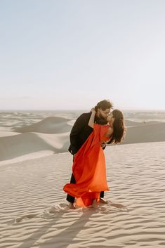 a man and woman kissing in the desert with sand dunes in the backgroud