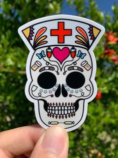 a hand holding up a sticker with a skull wearing a cross on it's head