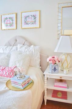 a white bed topped with lots of pillows next to a table filled with books and flowers